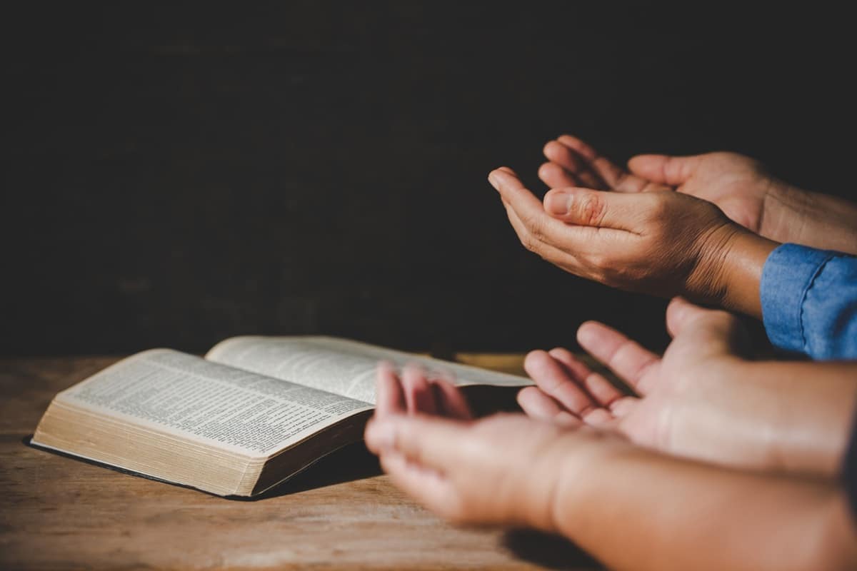 Mãos em oração diante de uma bíblia, simbolizando a espiritualidade e a religiosidade