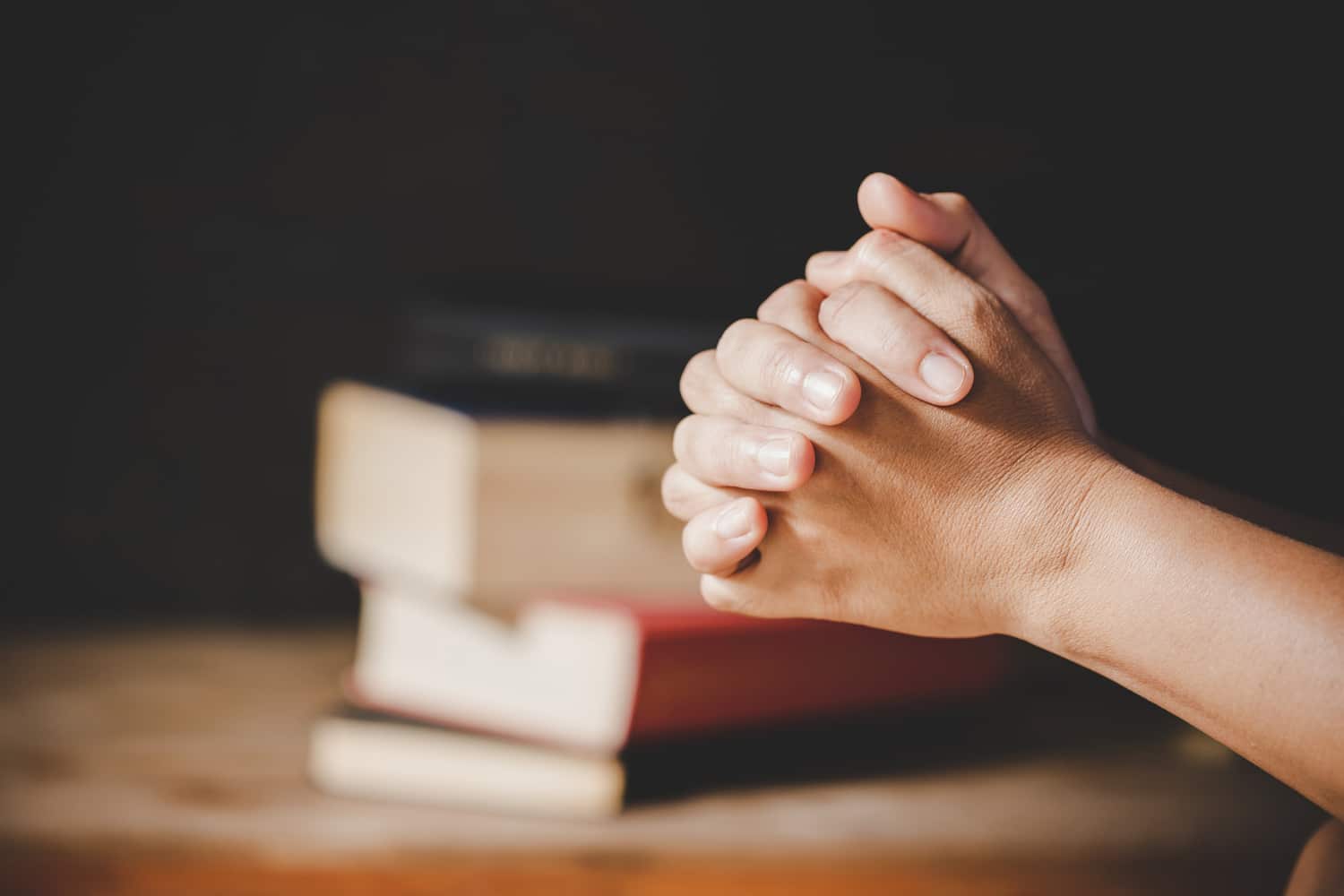 Mãos em oração diante de livros, simbolizando os estudos científicos sobre espiritualidade.