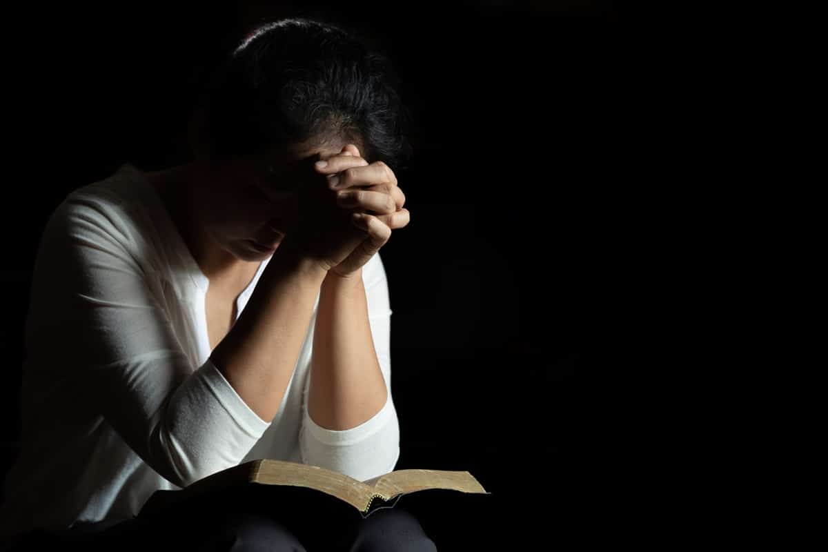 Mulher com as mãos juntas, em oração, com foco em sua fé como aliada no tratamento.