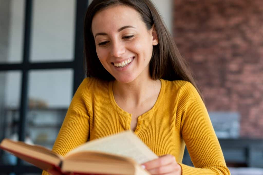 Mulher sorrindo enquanto lê um livro, ilustrando o prazer da leitura.