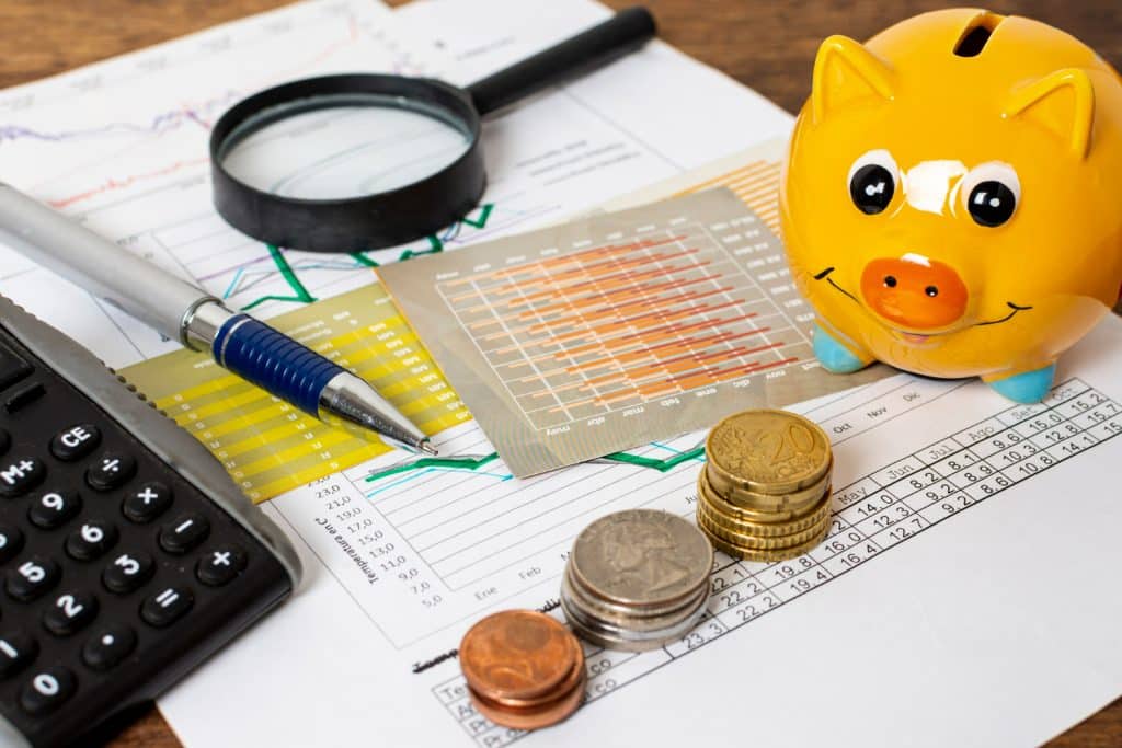 Cofrinho amarelo, moedas, gráficos, calculadora e lupa sobre papéis financeiros
