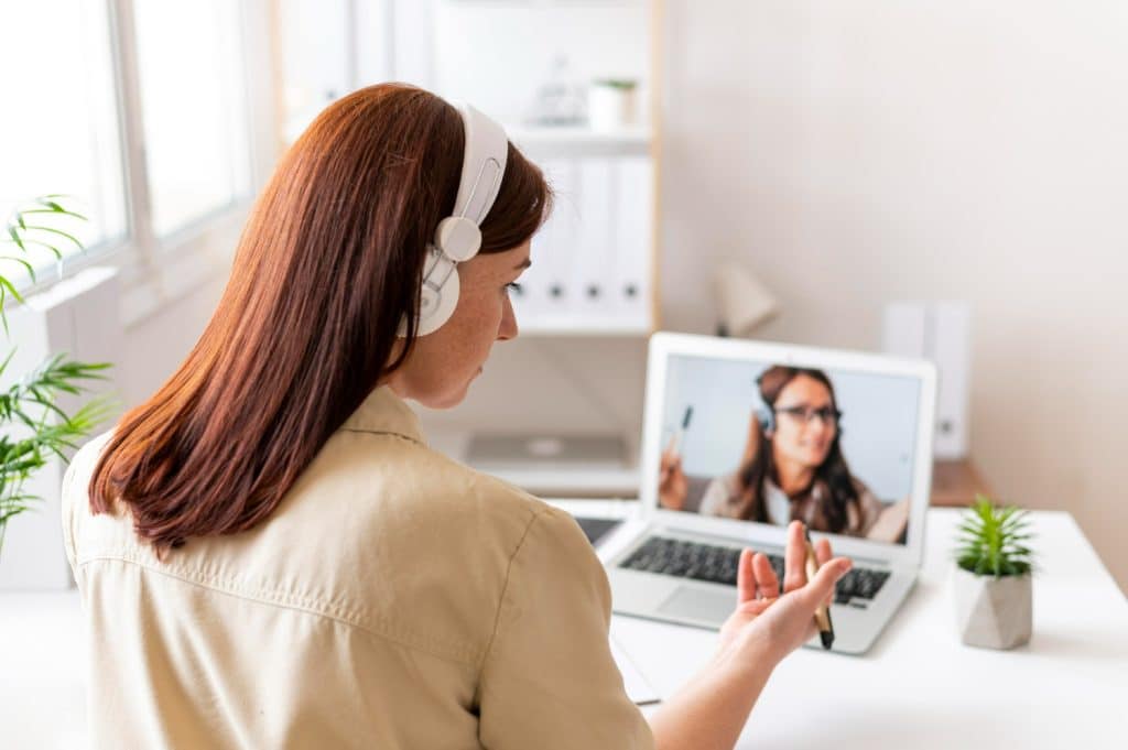 Mulher com fone de ouvido em videochamada com colega pelo notebook em escritório moderno.