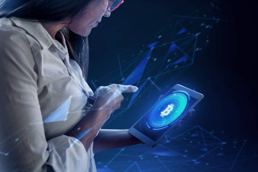 Mulher usando tablet com gráfico digital de bitcoin, representando o impacto do blockchain nas criptomoedas.