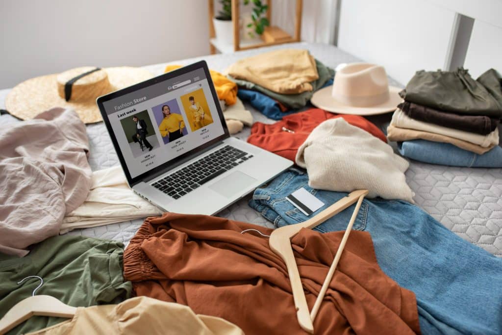  Notebook exibindo loja virtual de roupas femininas em meio a peças de roupa sobre a cama.
