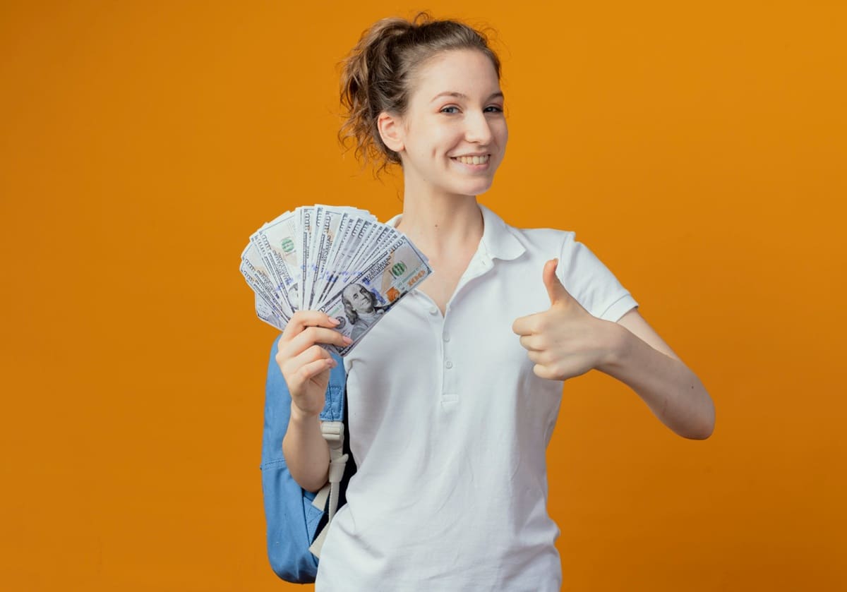 Imagem de um jovem estudando para concurso público, com um livro e caderno abertos, e um sorriso enquanto segura notas de 100 dólares.