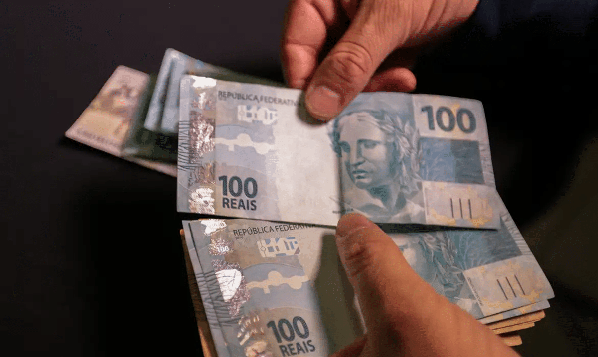 Pessoa contando cédulas de R$ 100, representando os pagamentos que serão feitos em agosto.