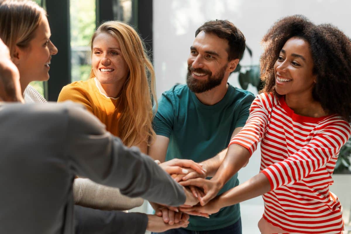 Grupo de amigos unidos com as mãos sobrepostas, simbolizando forte conexão social.
