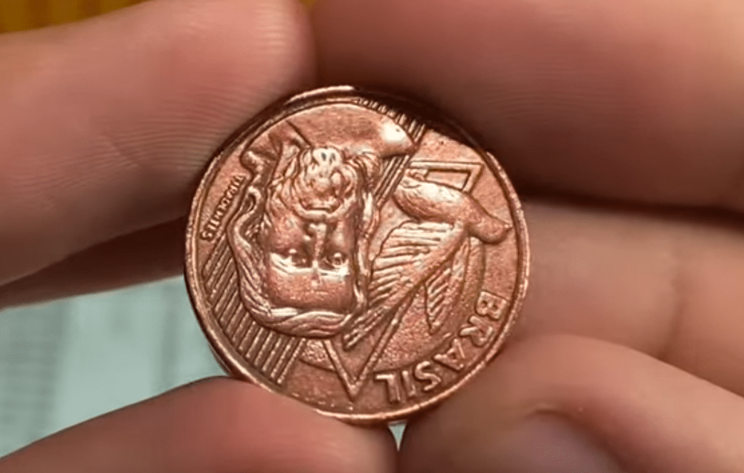 Moeda de 5 centavos com reverso invertido sendo exibida entre os dedos.