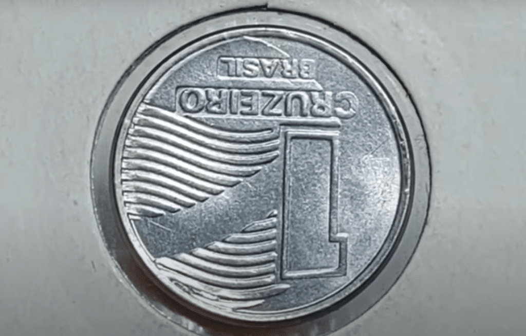 A moeda de 1 Cruzeiro de 1990 em close-up, mostrando a bandeira nacional.