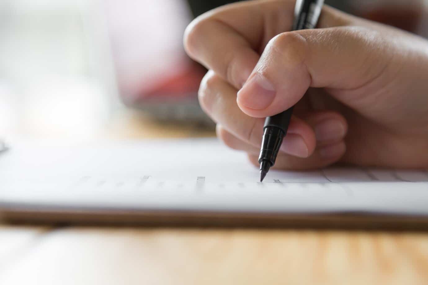 Pessoa preenchendo uma ficha de inscrição para um processo seletivo, com caneta e formulários em primeiro plano.