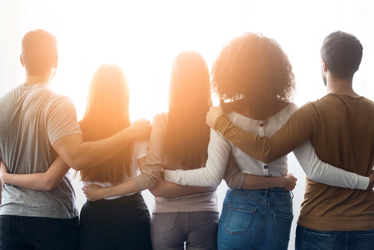 Cinco pessoas de costas, abraçadas, olhando para a luz, representando união e harmonia.