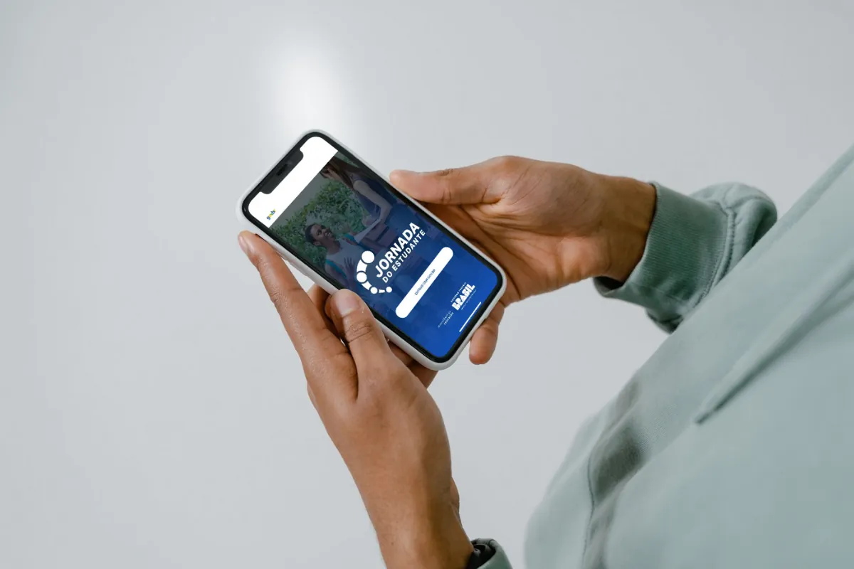 Pessoa segurando celular com o aplicativo Jornada do Estudante aberto na tela.