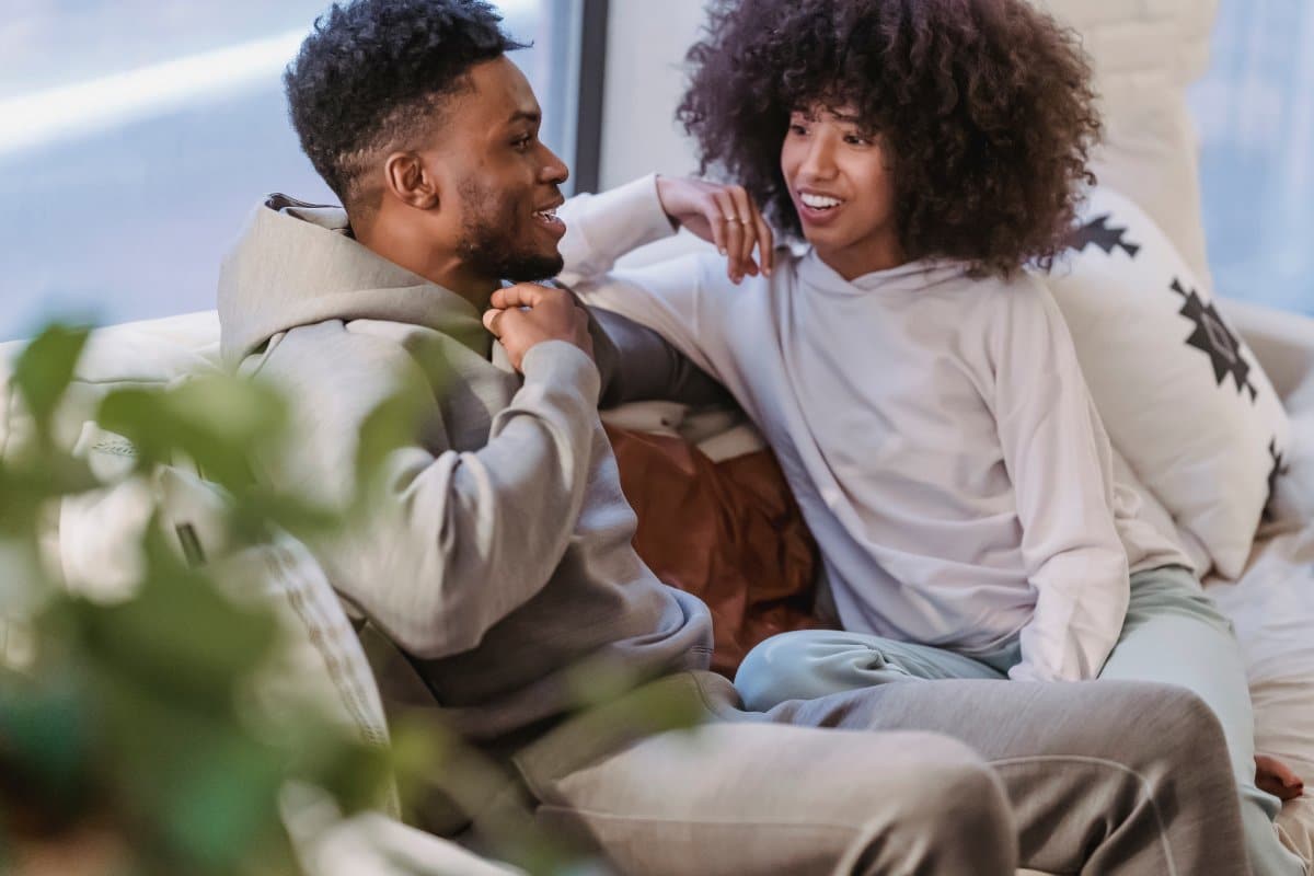 Casal sorridente conversando no sofá de forma descontraída.