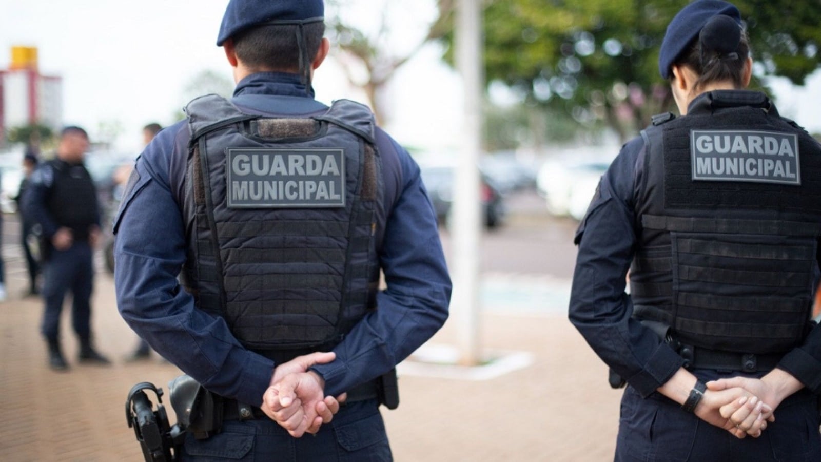 Guardas municipais uniformizados de costas durante patrulhamento.