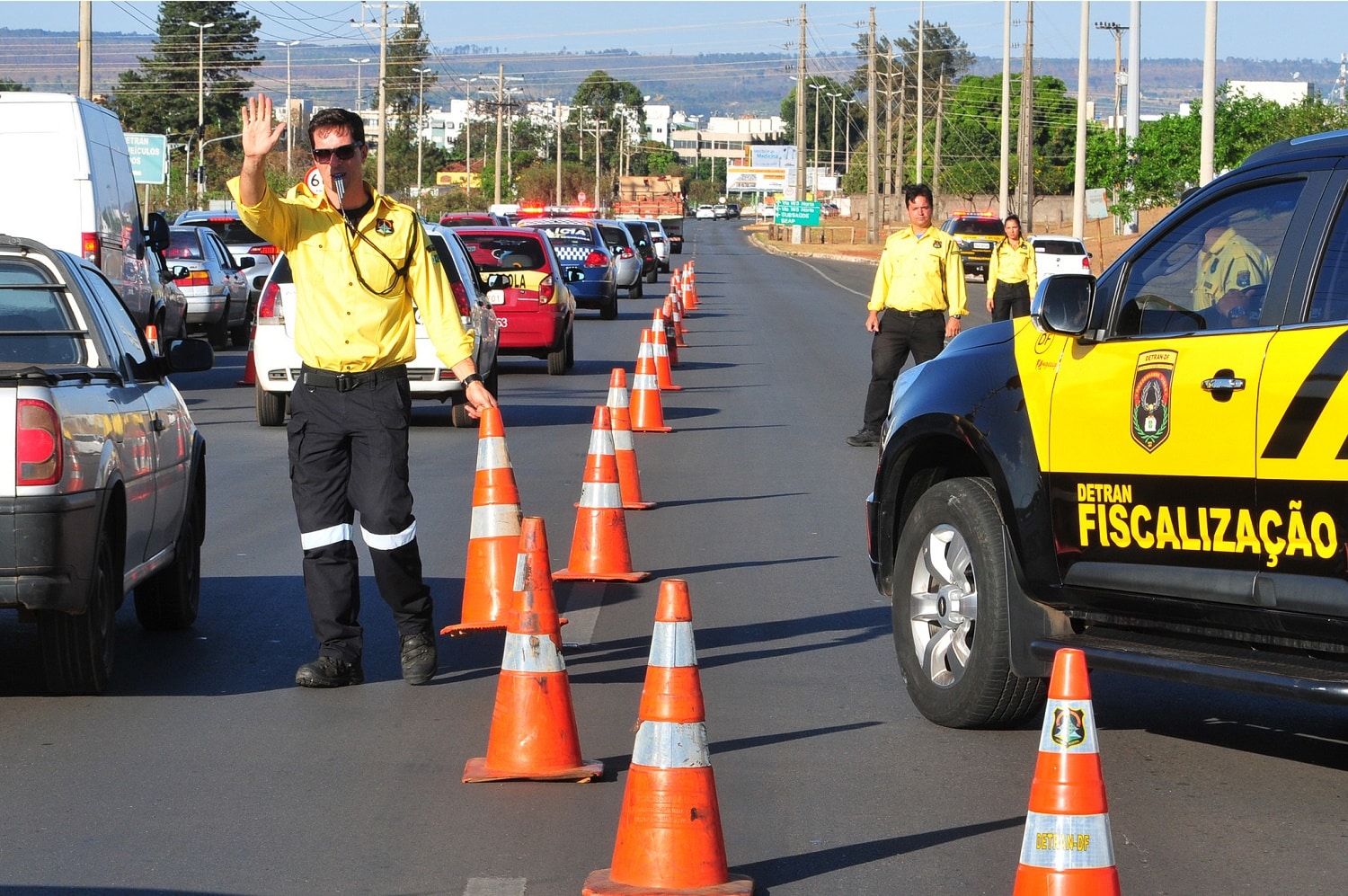 Agentes de fiscalização do Detran dirigindo um bloqueio de trânsito, com cones de sinalização em uma via pública.
