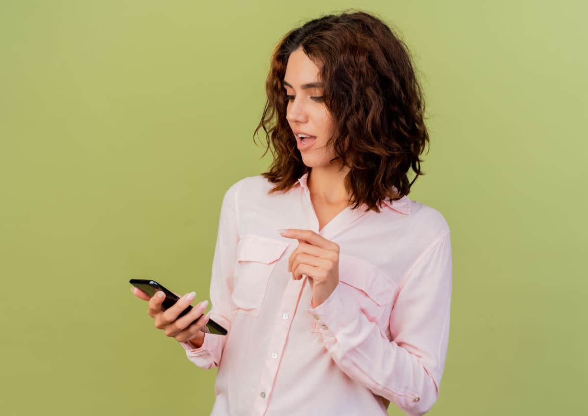 Mulher olhando surpresa para o celular, representando reação a status com indiretas no WhatsApp.