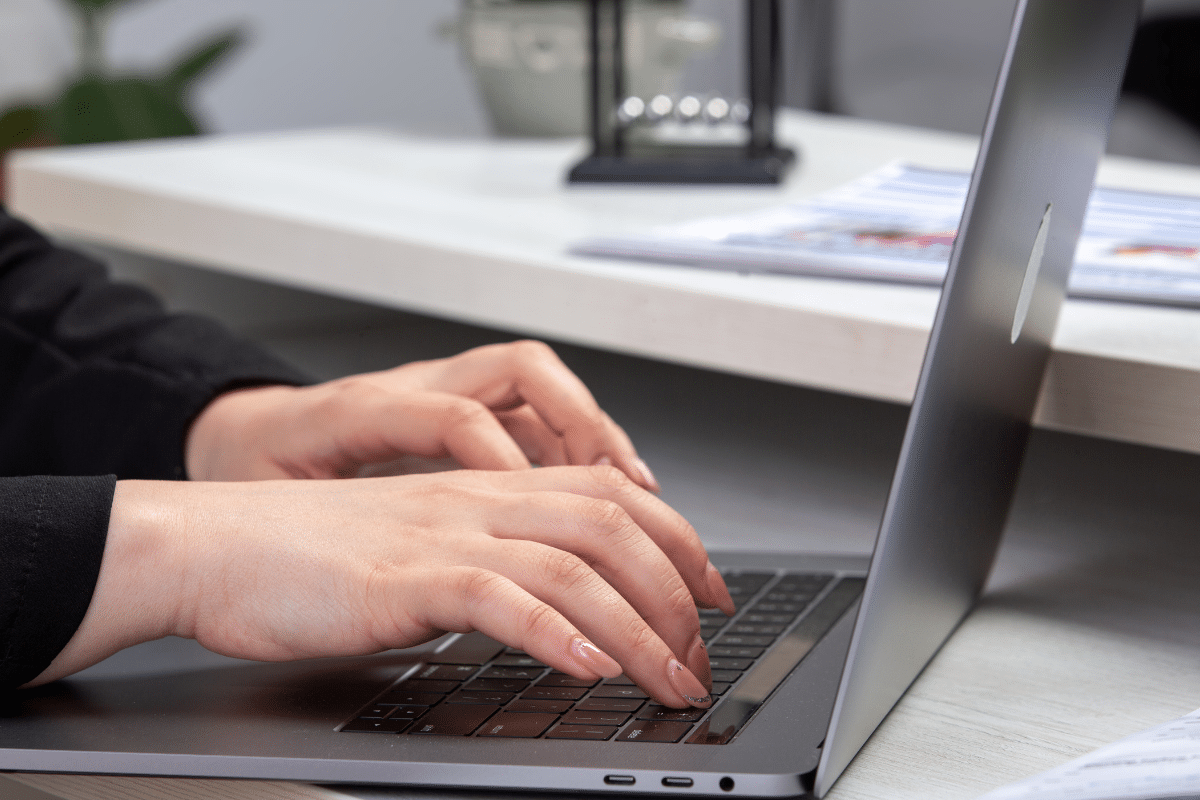 Mãos femininas digitando em teclado de notebook sobre mesa de escritório moderno.