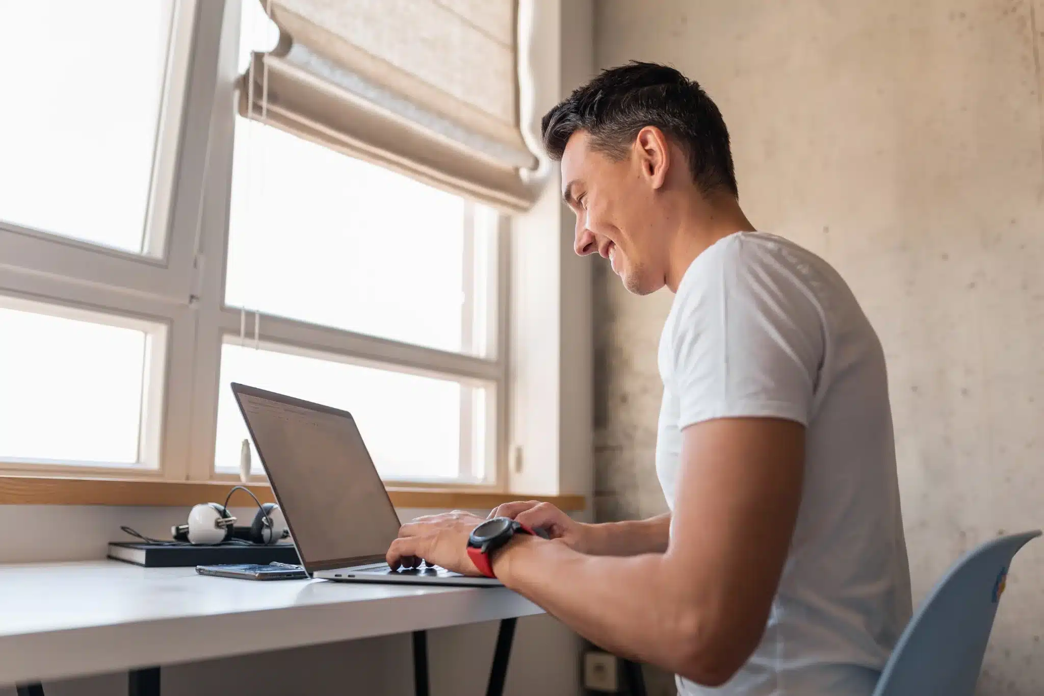 Homem sorrindo enquanto trabalha em um laptop, simbolizando a organização e preparação para o concurso.