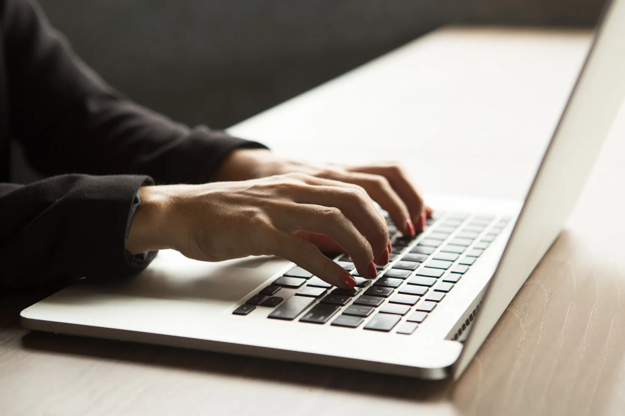 Mãos femininas digitando em notebook sobre mesa de madeira