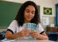 Estudante segurando notas de real em sala de aula, representando os pagamentos do programa Pé-de-Meia em agosto
