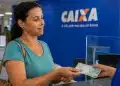 Mulher recebendo cédulas em uma agência da Caixa, representando o saque de até R$ 6.220 do FGTS a partir de 21 de julho.