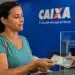 Mulher recebendo cédulas em uma agência da Caixa, representando o saque de até R$ 6.220 do FGTS a partir de 21 de julho.