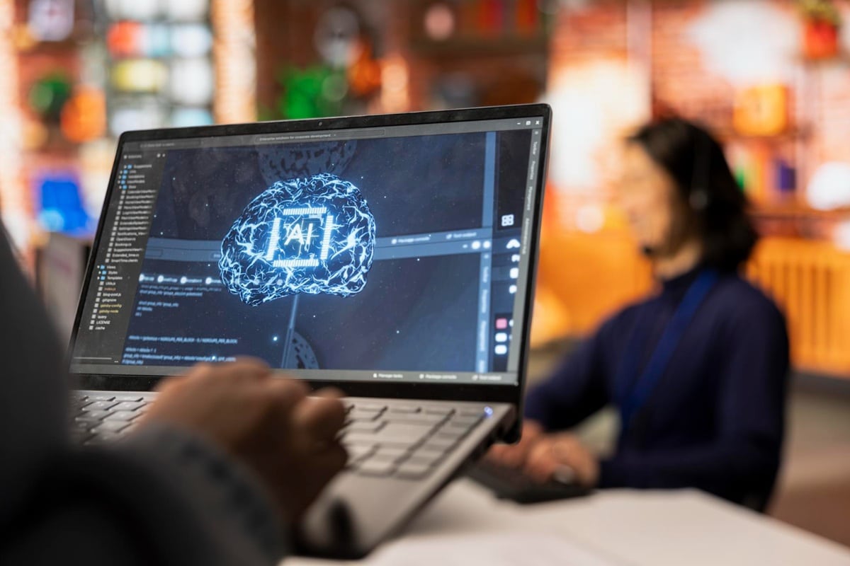 Laptop exibindo interface de inteligência artificial com cérebro digital luminoso e código de programação em ambiente de trabalho