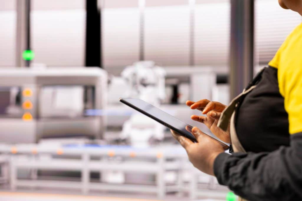 Trabalhador usando tablet para controle digital em ambiente industrial com equipamentos ao fundo.