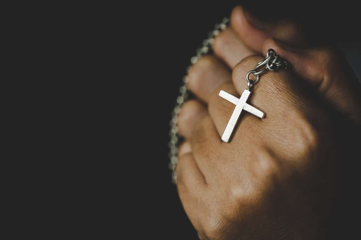 Mão segurando crucifixo prateado em corrente simbolizando proteção espiritual através da fé