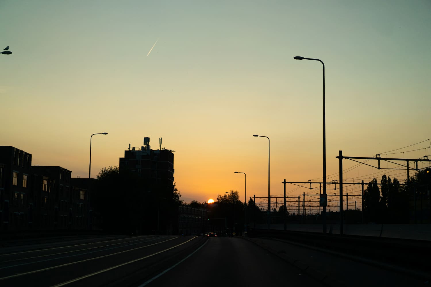 Vista do pôr do sol em uma área urbana com estrada, postes de luz e linhas de trem ao entardecer.