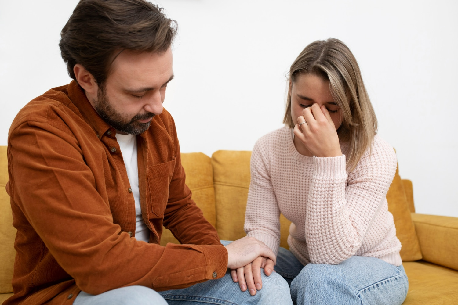 Homem confortando mulher triste segurando suas mãos em um sofá amarelo.