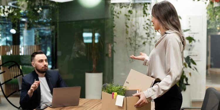 Mulher jovem segurando caixa de papelão com objetos pessoais em escritório moderno.