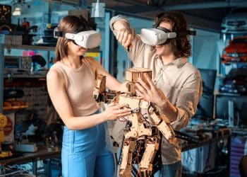 Dois jovens usando óculos de realidade virtual montando um robô de madeira com componentes eletrônicos em oficina tecnológica.