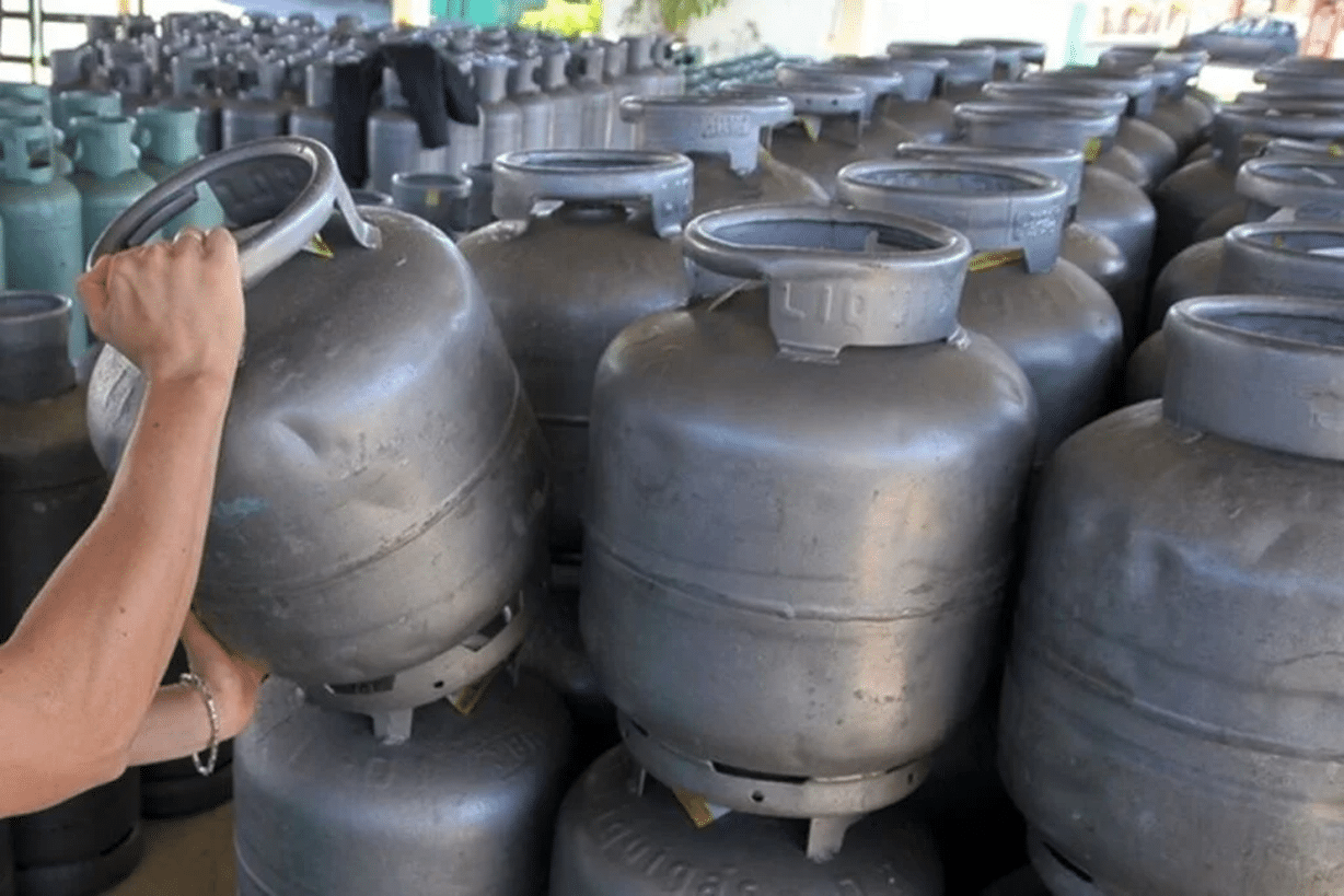 Pessoa levantando botijão de gás de cozinha entre vários botijões empilhados.