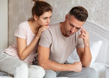 Mulher preocupada consolando homem pensativo e triste sentado na cama em quarto claro.