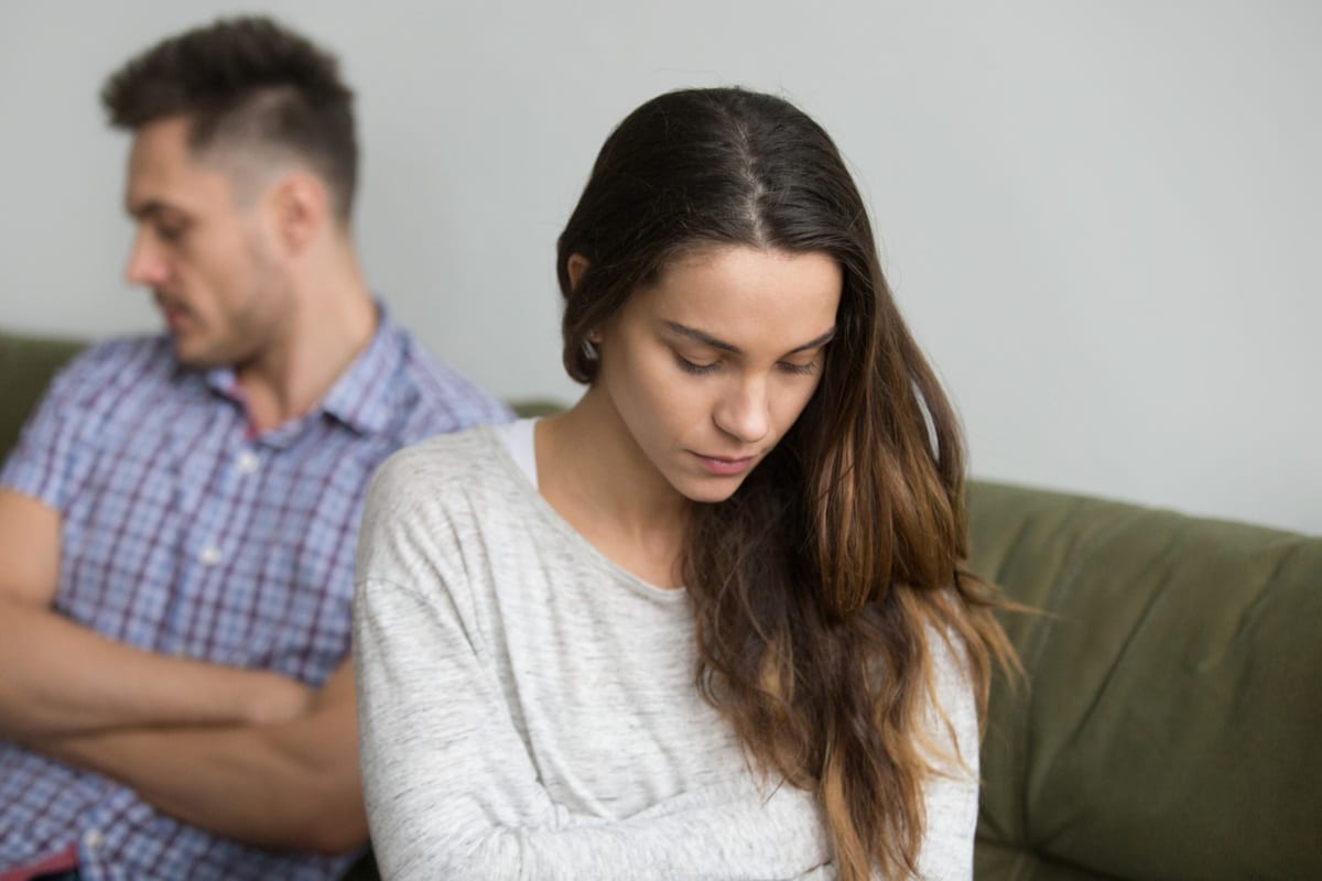 Casal demonstrando distanciamento emocional sentados em lados opostos do sofá evidenciando problemas de relacionamento