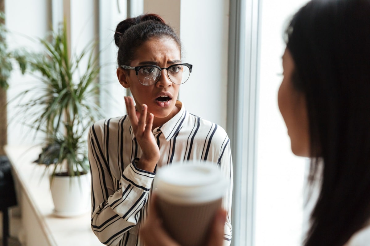 Mulher gesticulando enfaticamente durante conversa em café demonstrando expressão potencialmente interpretada como arrogante