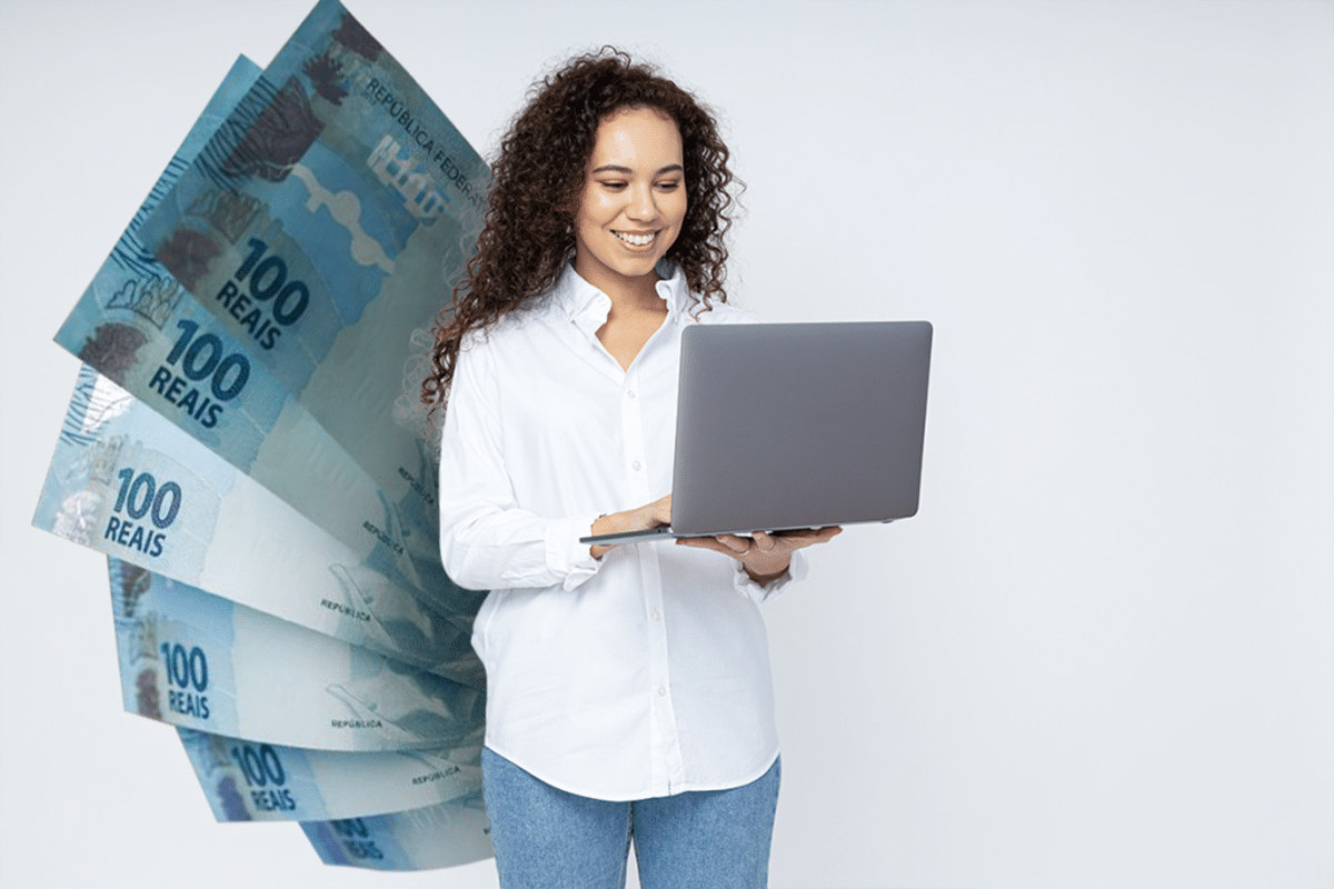 Mulher sorridente com camisa branca usando laptop, com notas de 100 reais flutuando ao fundo