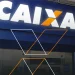 Fachada de agência da Caixa Econômica Federal com logo iluminado em azul e branco à noite.