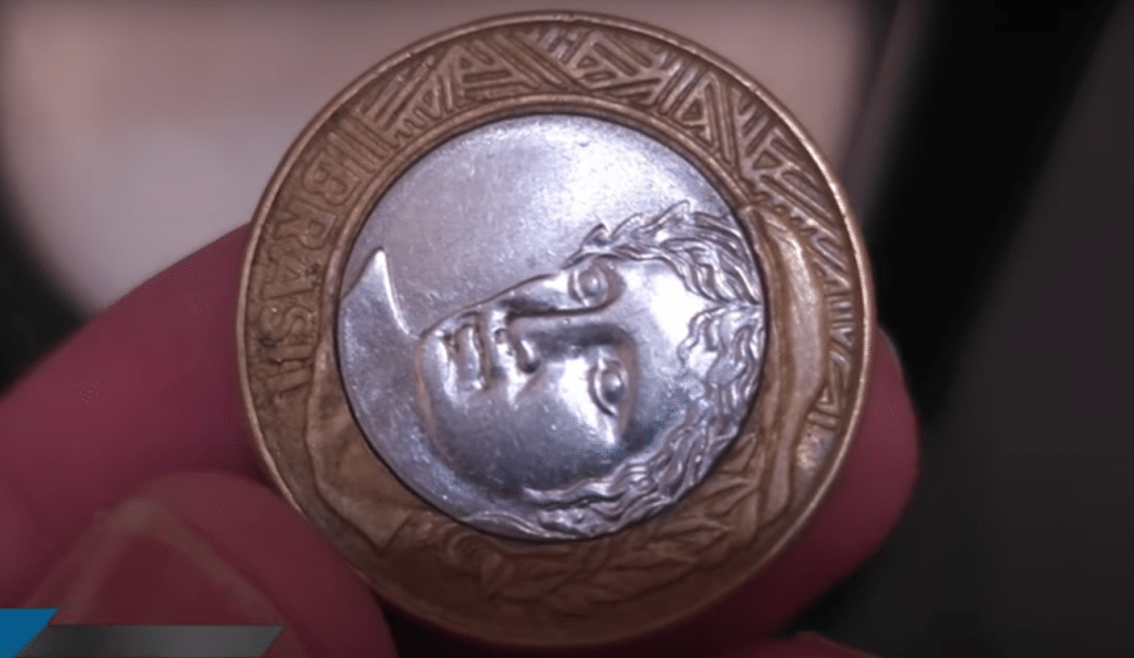 Moeda de 1 real com reverso invertido horizontalmente, mostrando a efígie deitada para a esquerda.