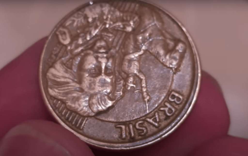 Moeda brasileira de 10 centavos sendo segurada por uma mão, com o reverso invertido (de cabeça para baixo), destacando o erro de cunhagem que a torna rara e valiosa.