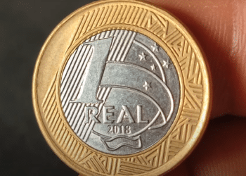 Moeda de 1 real de 2018 sendo segurada, mostrando o anverso com o valor e o ano.