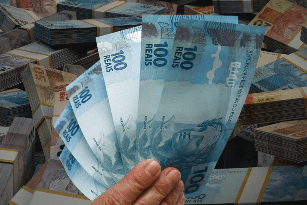 Pessoa mostrando três notas de cem reais com maços de dinheiro organizados ao fundo representando benefícios financeiros