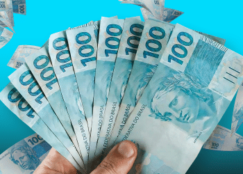 Mão segurando leque de oito notas de cem reais sobre fundo azul representando pagamento governamental