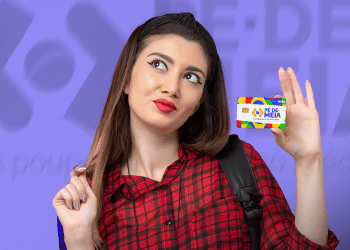 Jovem segurando cartão Pé de Meia colorido com sorriso pensativo, vestindo camisa vermelha xadrez.