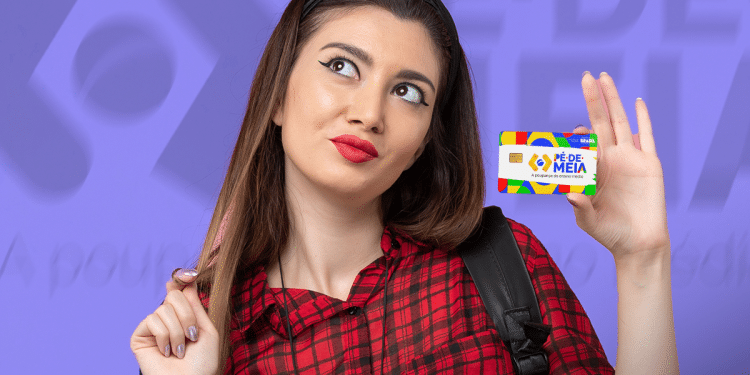 Jovem segurando cartão Pé de Meia colorido com sorriso pensativo, vestindo camisa vermelha xadrez.