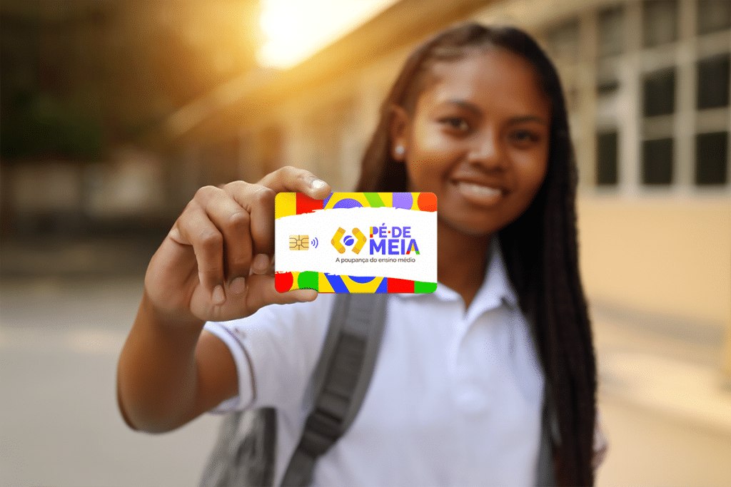 Adolescente sorridente mostra cartão Pé de Meia com design colorido ao ar livre.