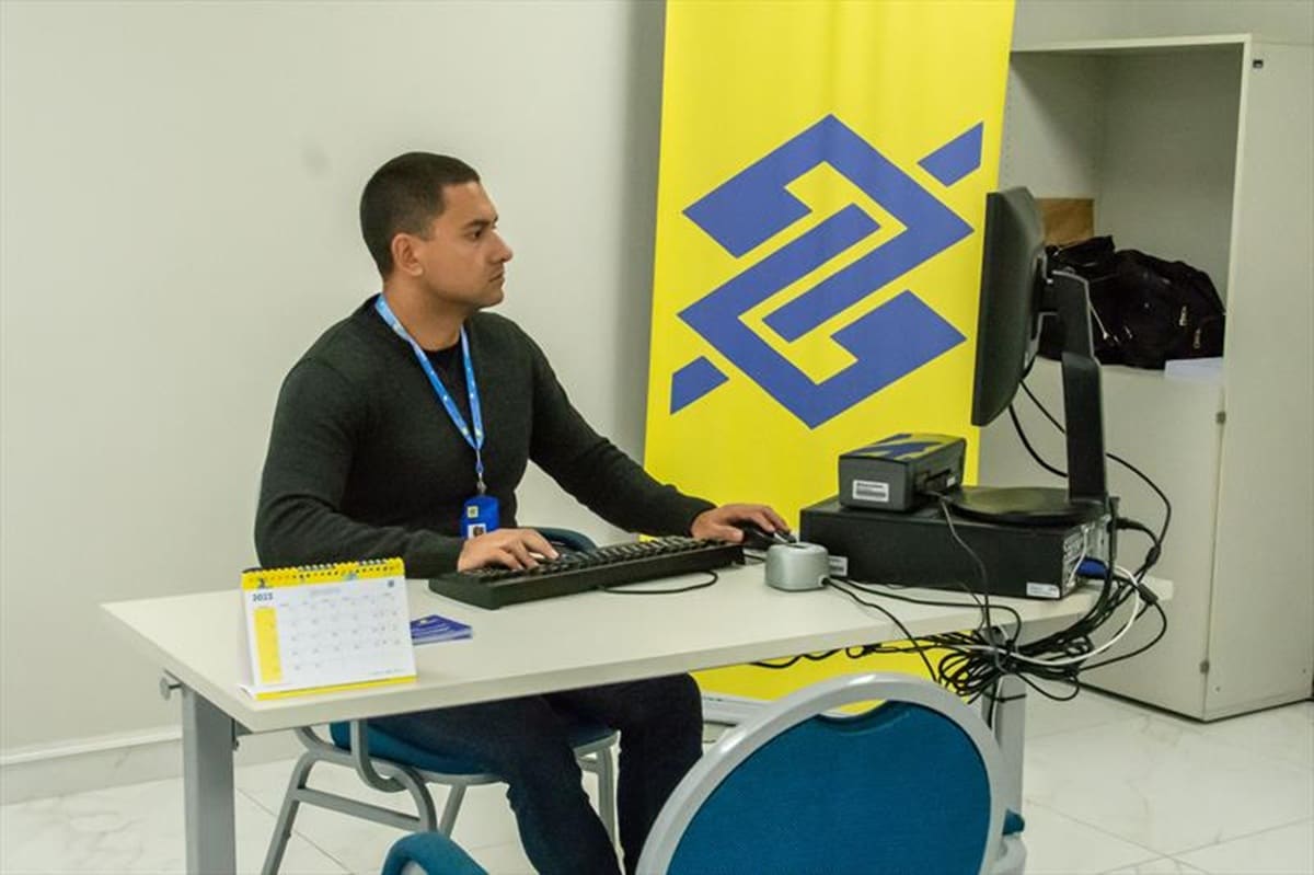 Funcionário do Banco do Brasil trabalhando em computador na agência com uniforme e crachá da instituição