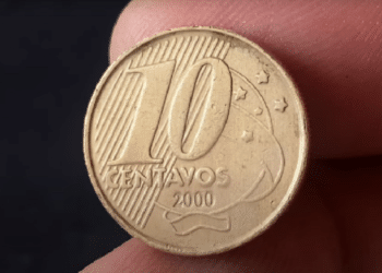 Uma moeda brasileira de 10 centavos do ano 2000, segurada entre os dedos, mostrando a data de cunhagem e o busto de Tiradentes no reverso.