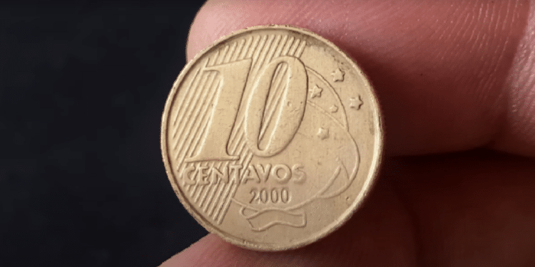 Uma moeda brasileira de 10 centavos do ano 2000, segurada entre os dedos, mostrando a data de cunhagem e o busto de Tiradentes no reverso.